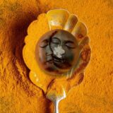 A handcrafted, deep ochre-colored soap bar with a rustic, uneven top edge, resting on a textured linen cloth. The soap, titled 'The Golden Glow,' is surrounded by whole turmeric roots and a dusting of golden powder. The lighting is warm and cinematic, emphasizing the earthy, artisanal texture of the bar and creating a serene, spa-like atmosphere.