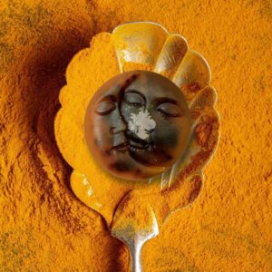 A handcrafted, deep ochre-colored soap bar with a rustic, uneven top edge, resting on a textured linen cloth. The soap, titled 'The Golden Glow,' is surrounded by whole turmeric roots and a dusting of golden powder. The lighting is warm and cinematic, emphasizing the earthy, artisanal texture of the bar and creating a serene, spa-like atmosphere.