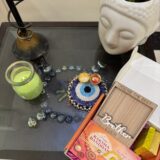 Centered is a beaded evil eye coaster with two small traditional katoris (bowls) holding roli and chawal. To the right is an open orange gift box containing purple shred, a 'Happy Raksha Bandhan' greeting card with a red and yellow thread rakhi, a small gold bar, and a wooden photo frame etched with 'YOU'RE THE BEST' and 'Brother EVER'.